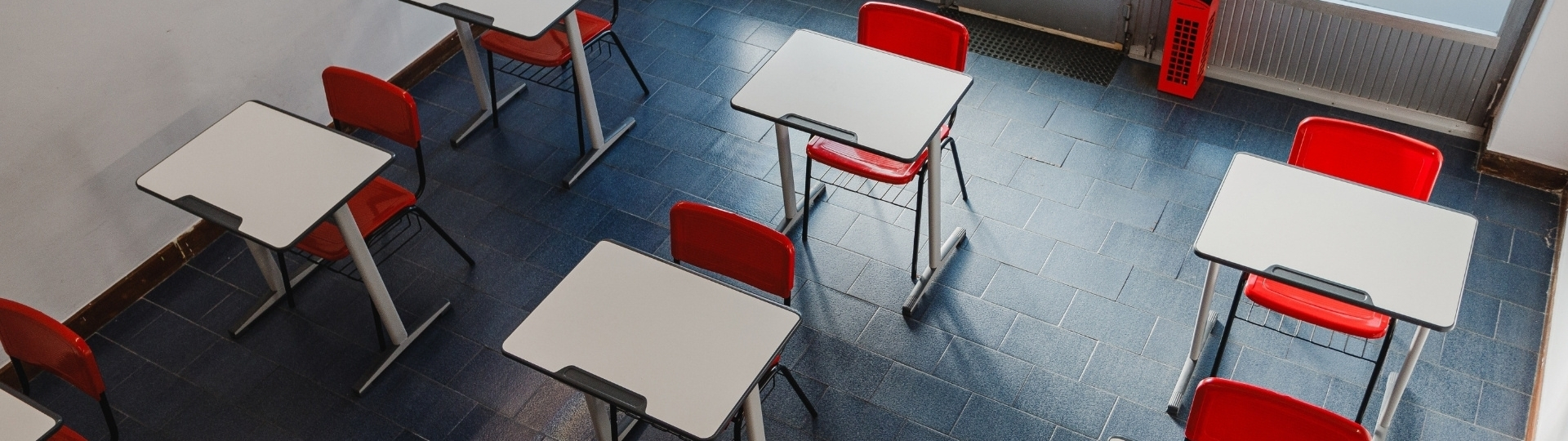Aula de clases de inglés para adultos en The Real Academy Of English con pupitres blancos, sillas rojas y suelo azul vista desde arriba